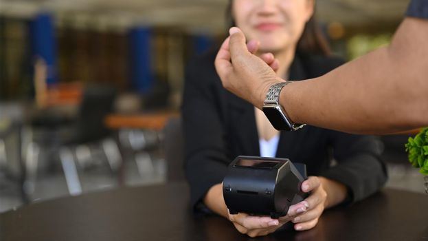 Cropped image of customer paying through smart watch at coffee shop.