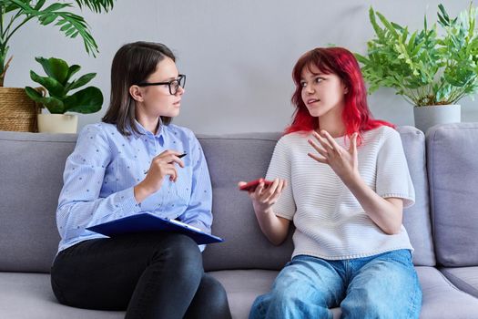 Psychologist counseling teenage female, individual therapy in doctors office. Professional counselor helping teenager, girl with smartphone. Mental health, adolescence, psychology, psychiatry concept