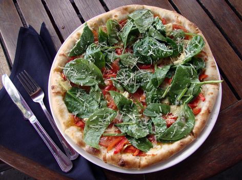 Spinach Margarita Pizza with a fork and knife on top of a napkin on an outdoor table.