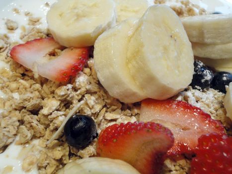 Granola close-up with Fresh Fruit including slices of Strawberries, bananas, and blueberries.