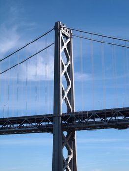 San Francisco Bay Bridge Tower with double deck road and cables on a clear blue day with little clouds.