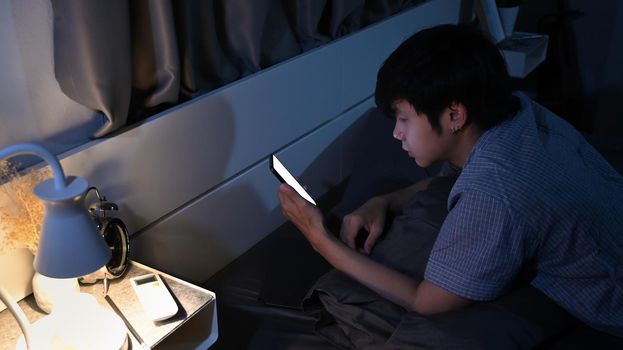 Young man laying on comfortable bed and using smart phone.