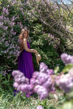 Fashion Model in Lilac Flowers, Young Woman in Beautiful Long Dress Waving on Wind, Outdoor Beauty Portrait in Blooming Garden.