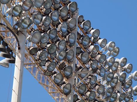 Stadium-style lights viewed close up, taken at Oakland Colisuem looking forward, clear blue sky background, during the daytime so the lights are off.