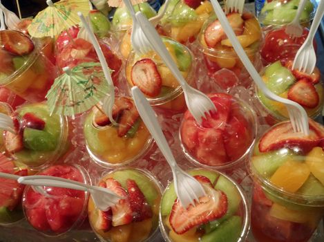 Plastic Fruit cups with forks placed in the top on display in a tray filled with ice.