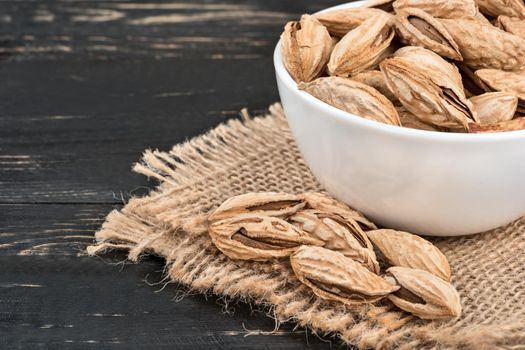 Uzbek inshell almonds in bowl on a burlap and wood background closeup