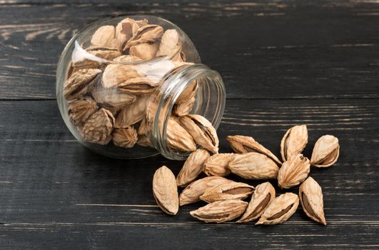 Scattered uzbek almonds from a jar on a dark table