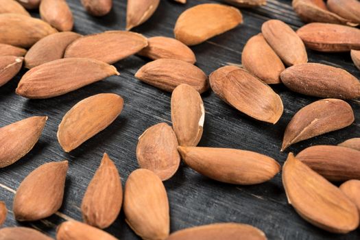 Scattered Uzbek almonds without shell on wooden background, closeup