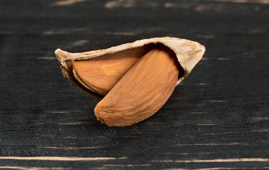 Uzbek open inshell almonds on wooden background, closeup