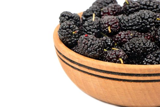 Part of a wooden bowl of black mulberries on a white background