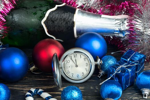 Christmas balls, decorations, bottle of champagne and watch on wooden background