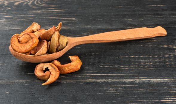 Slices of dried apples in a spoon on wooden background