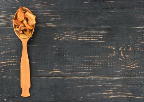 Dry apple slices in the empty spoon on wooden background
