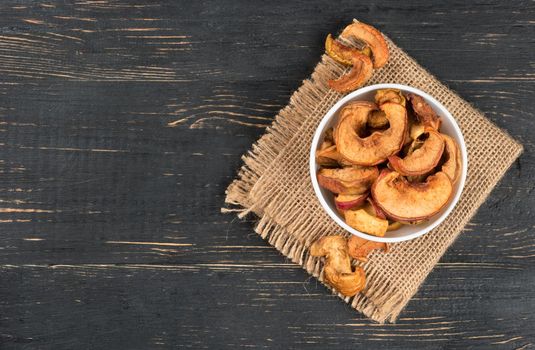 Bowl of dry Apple slices on sackcloth and wooden background, top view