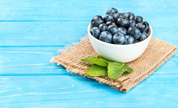 Full bowl of fresh blueberries with mint leaves on sackcloth and table