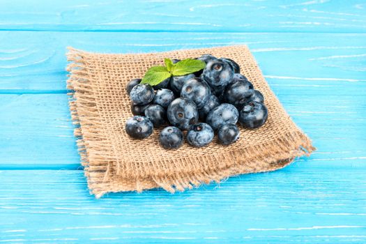 Small pile of ripe blueberries with mint leaves on sackcloth and table