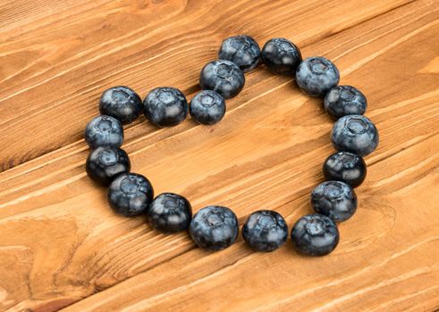 Fresh blueberries lined with in heart shape on wooden background
