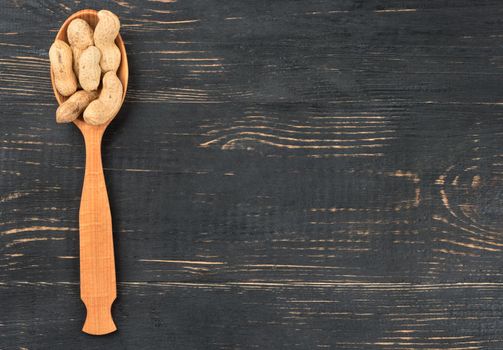 Dry peanuts in a shell in a spoon on an empty wooden background