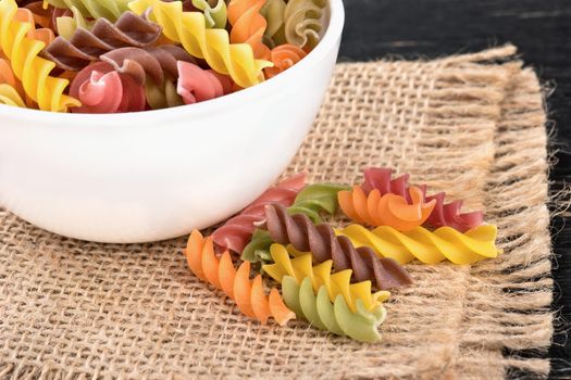 Raw colored pasta fusilli with a bowl closeup