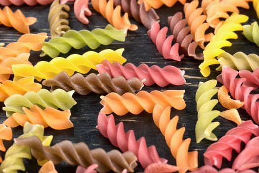 Scattered multi-colored raw pasta fusilli on wooden background