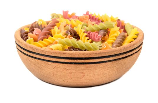 Colored pasta fusilli in a wooden bowl on white background