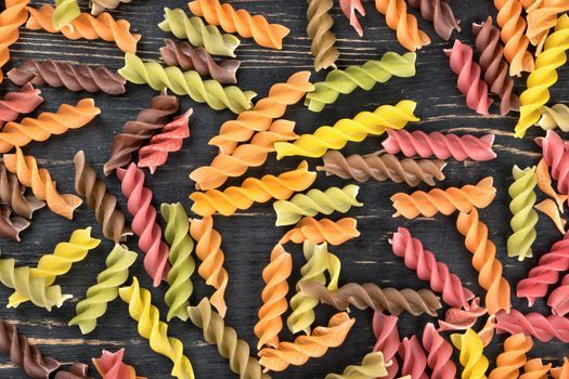 Scattered multi-colored raw pasta fusilli on wooden background