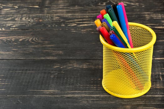 Colored markers in the empty basket on wooden background