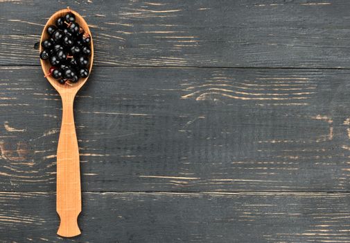 Bird cherry in spoon on empty wooden background, top view