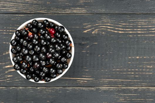 White bowl of bird cherries on an empty wooden background, top view