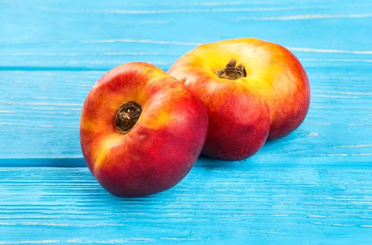 Two ripe flat peaches on blue table