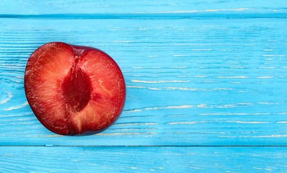 Half of a delicious red plums on an empty wooden background, top view
