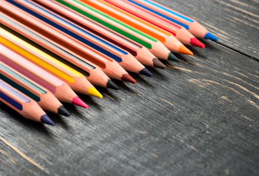 Scattered colored pencils on a dark wooden background, closeup