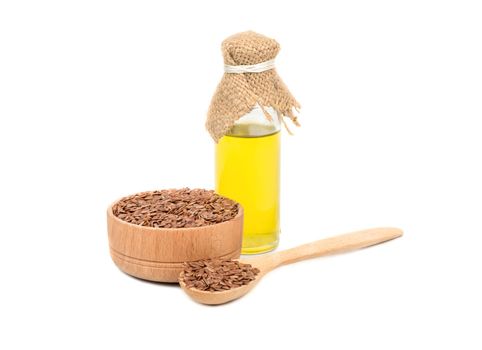 Bowl, spoon with seeds and a bottle of linseed oil on white background