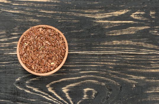 Flax seeds in the empty bowl on wooden background, top view