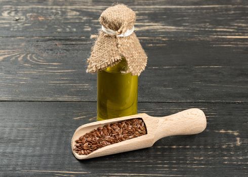 Linseed oil in a bottle with beans in the scoop on wooden background