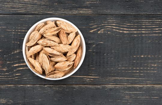 Ceramic bowl filled with Uzbek inshell almonds on wooden background