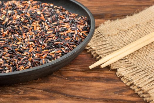 Part of frying pan with wild rice and chopsticks on wooden background