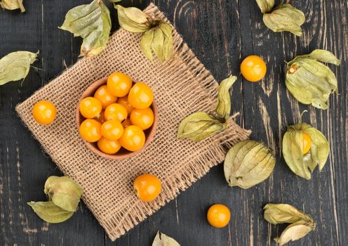 Bowl with physalis and scattered berries on wooden background, top view