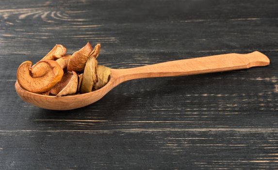 Slices of dried apples in a spoon on wooden background