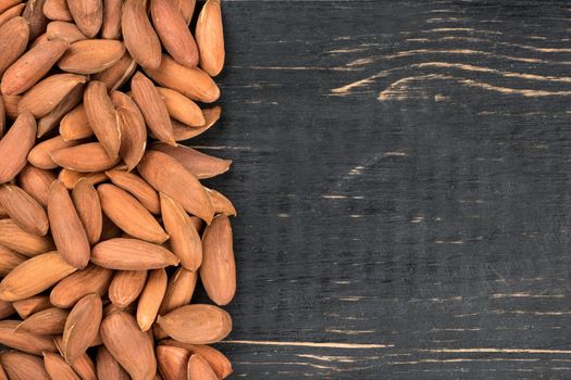 Scattered Uzbek almonds without the shell on an empty wooden background, top view