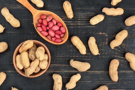 Peanuts in shell in a spoon, bowl and scattered on a wooden background, top view