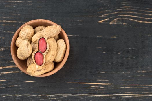 Small bowl with peanuts in the shell on wooden background, top view