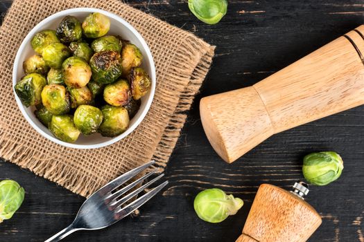 Fried brussels sprouts in bowl with ingredients on the table, top view