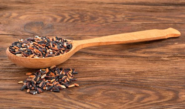 Spoon with raw black rice on the table close-up