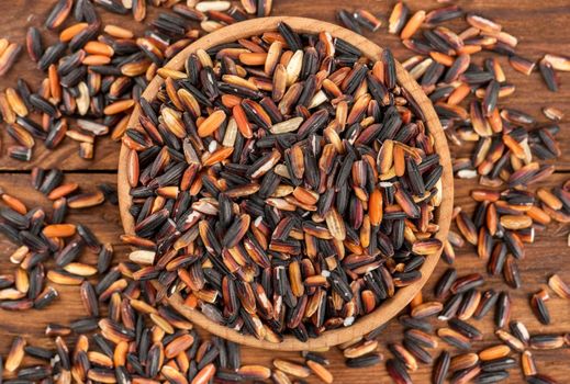 Black rice in a small bowl on a wooden background top view