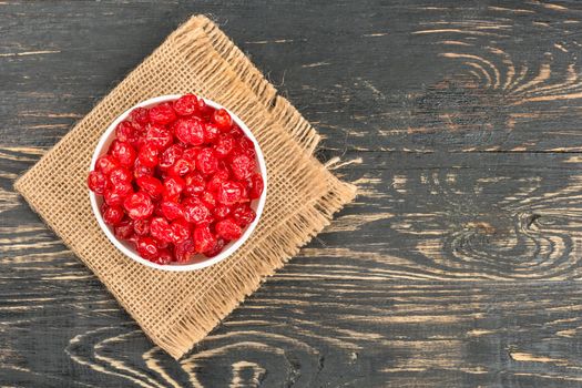 Dry cherries in a bowl and burlap empty on wooden background