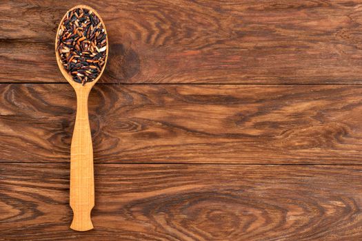 Wild rice in spoon on empty wooden background