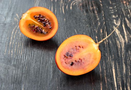 Two halves tamarillo fruit on wooden background close-up
