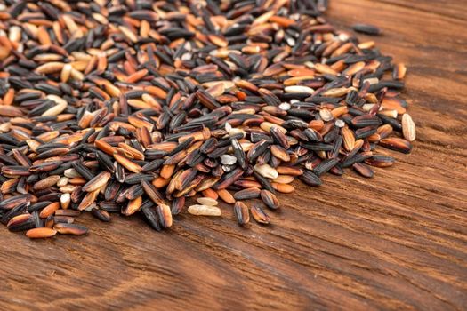 Scattered black wild rice on wooden background close up