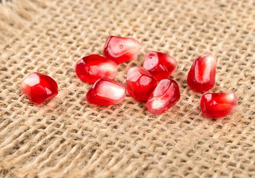 Ripe pomegranate seeds scattered on sackcloth closeup